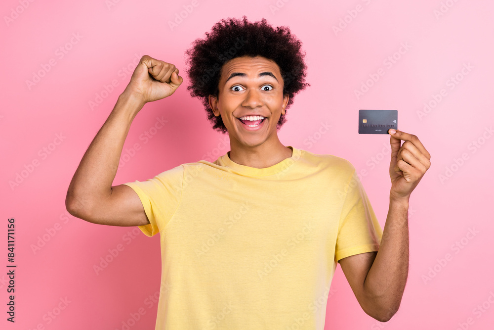 Photo of delighted positive man raise fist hold debit plastic card isolated on pink color background Photo of delighted positive man raise fist hold debit plastic card isolated on pink color background