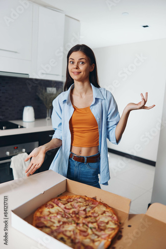 Young woman standing in front of a large pizza box with her hands outstretched in anticipation