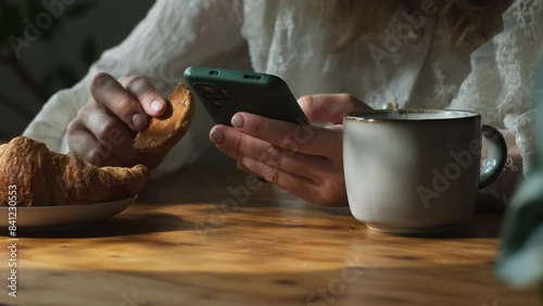 Coffee break. Woman uses smartphone and drinks coffee at breakfast in morning photo