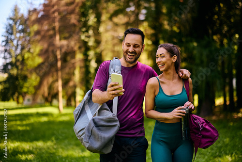 Happy athletic couple using app on mobile phone in park.