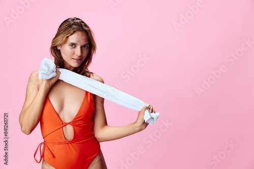 Vibrant woman in orange swimsuit holding towel against pink backdrop in sunny summer scene