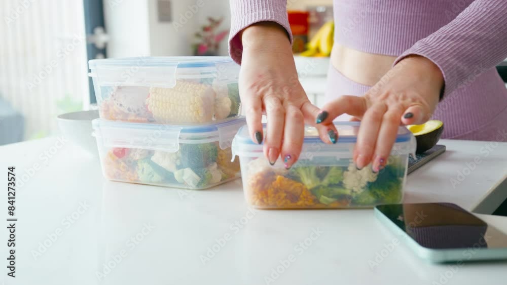 Close up of woman wearing fitness clothing at home in kitchen making up batch of healthy meals for freezer in plastic containers - shot in slow motion Close up of woman wearing fitness clothing at home in kitchen making up batch of healthy meals for freezer in plastic containers - shot in slow motion