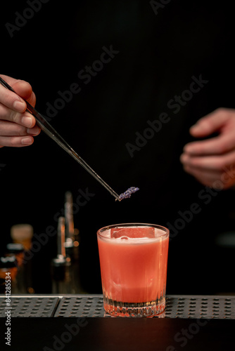 close-up of beautiful crystal glass with pink alcoholic drink which man decorates with sprig of violet flower