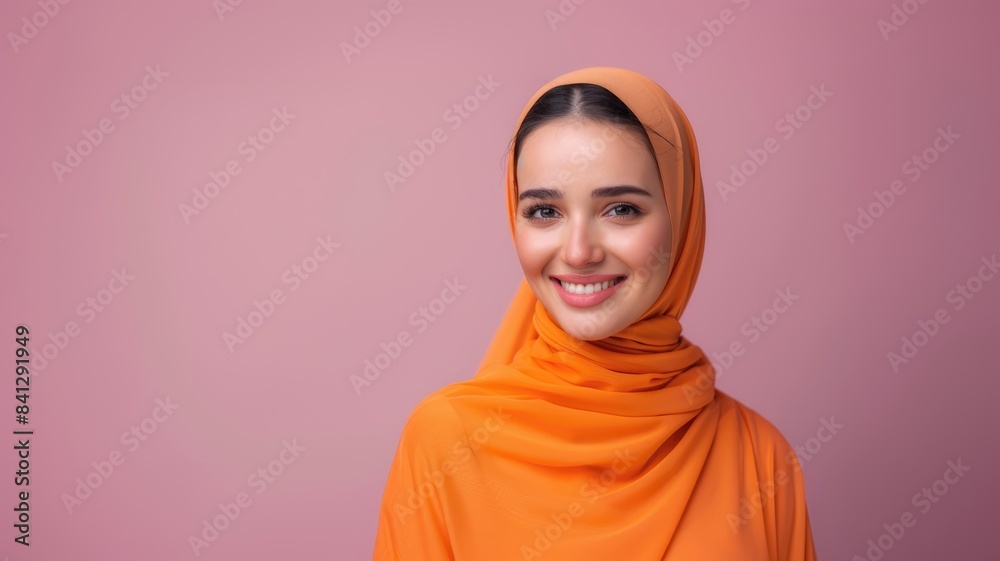 Young smiling beautiful arabian asian muslim woman wear orange abaya hijab look camera isolated on plain light pink color background studio portrait. People uae middle eastern islam religious concept.