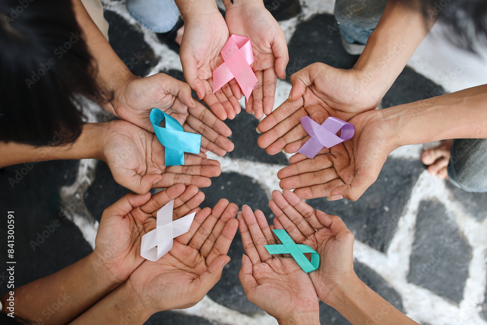 Fototapeta premium World cancer day. Hands of people open and holding colourful awareness ribbons forming circle as unity for supporting people living and illness.