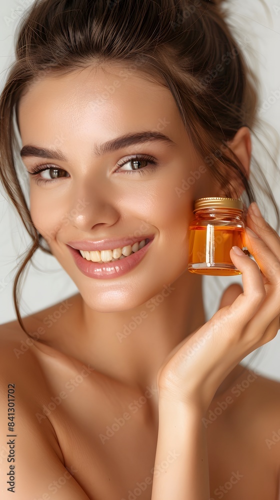 Fototapeta premium Beautiful smiling young woman with clean skin holding facial essential oil or serum with dropper, rejuvenation and skin care, white background