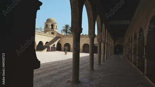 View from shaded archway gallery to sunlit courtyard of Great Mosque of Sousse and small domed corner tower rising against blue clear sky, showcasing traditional Islamic architecture. High quality 4k photo