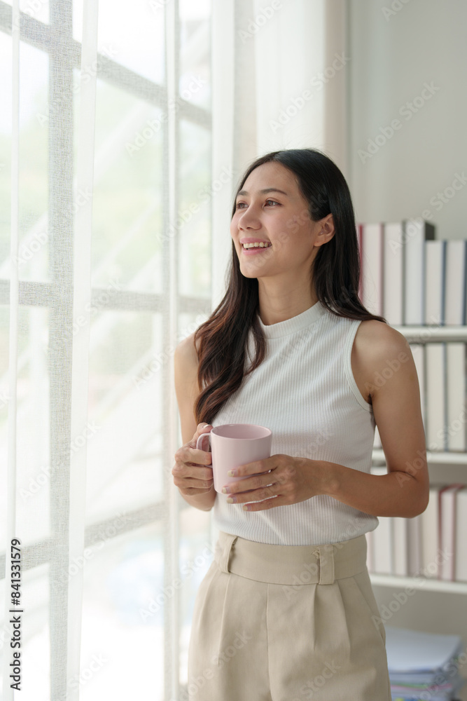 Young Asian woman working on laptop and drinking coffee in living room relaxing at home. Asian business woman working with financial documents Calculator, calculations, holiday concept at work.