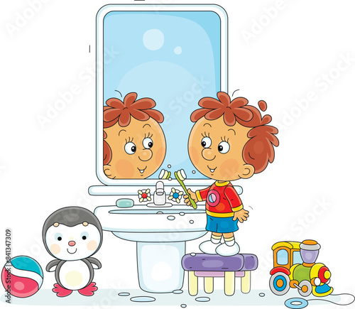 Funny little boy brushing his teeth at a mirror and washbasin in a bathroom with toys, vector cartoon illustration isolated on a white background