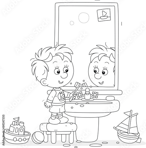 Funny little boy brushing his teeth at a mirror and washbasin in a bathroom with toys, black and white vector cartoon illustration for a coloring book