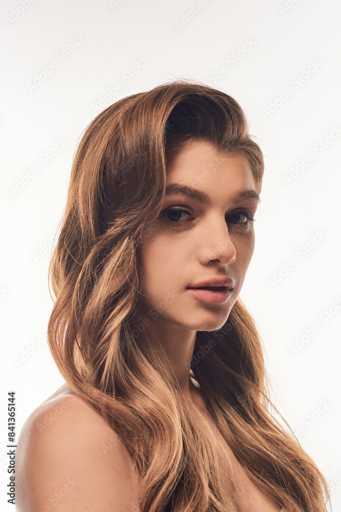 Fototapeta premium A young woman with long, wavy hair poses gracefully for a portrait.