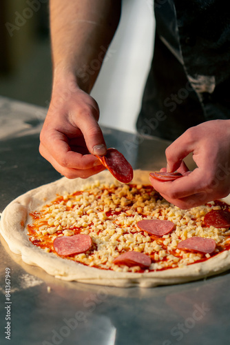close up in a professional kitchen in a pizzeria young chef in a black uniform puts ingredients on pizza