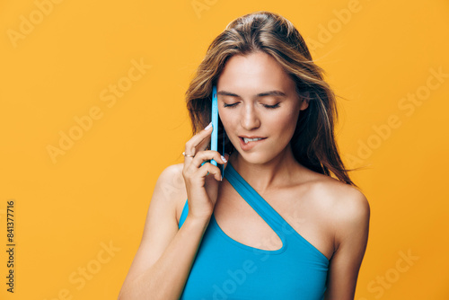 Vibrant image of a stylish woman in blue top talking on cell phone with bright yellow background