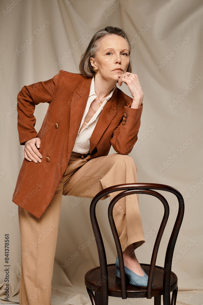 Mature woman poses actively in tan blazer and pants on chair. Stock ...