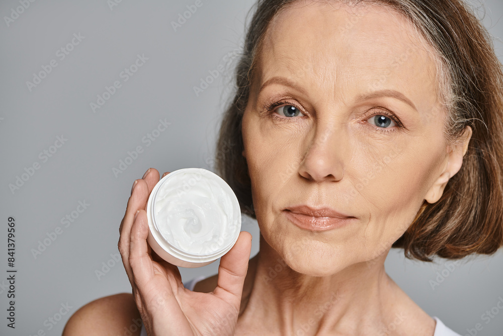 A mature woman in comfortable attire elegantly holding a container of cream. A mature woman in comfortable attire elegantly holding a container of cream.