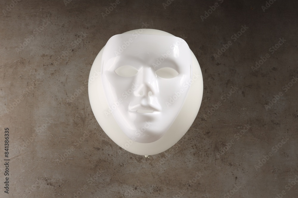 Theatrical performance. Plastic mask and white balloon on grey table, top view Theatrical performance. Plastic mask and white balloon on grey table, top view