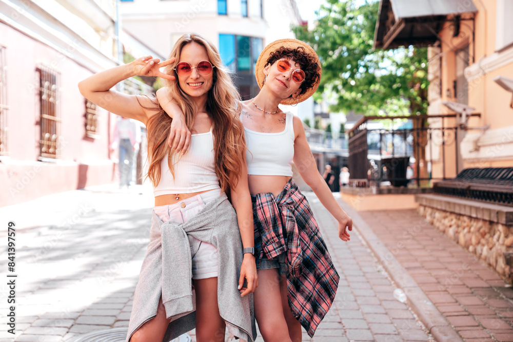 Naklejka premium Two young beautiful smiling hipster female in trendy summer white t-shirt and shorts clothes. Sexy carefree women posing in the street. Positive models having fun, hugging and going crazy