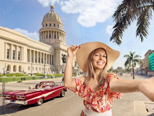Photography Smiling young female tourist in a dress and straw hat taking a selfie on the str