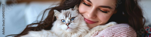 A woman with long brown hair holds a white cat with blue eyes in her arms indoors