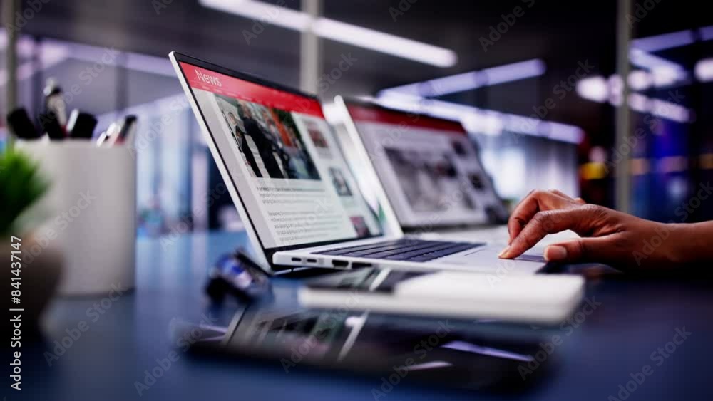 American Woman Views Online News Articles on Laptop and Phone While Relaxing on Sofa in Black American Woman Views Online News Articles on Laptop and Phone While Relaxing on Sofa in Black