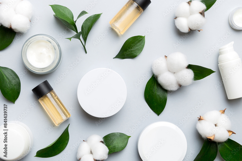 Organic cosmetic products with cotton flower and green leaves on color background. Flat lay