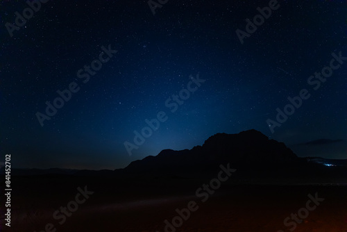 Captivating night sky  sprinkled with stars sets over the silhouette of Jabal al Qattar rock formation in the tranquil Wadi Rum desert in Jordan in April