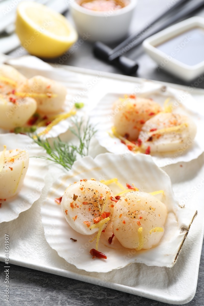 Raw scallops with spices, dill, lemon zest and shells on grey marble table, closeup