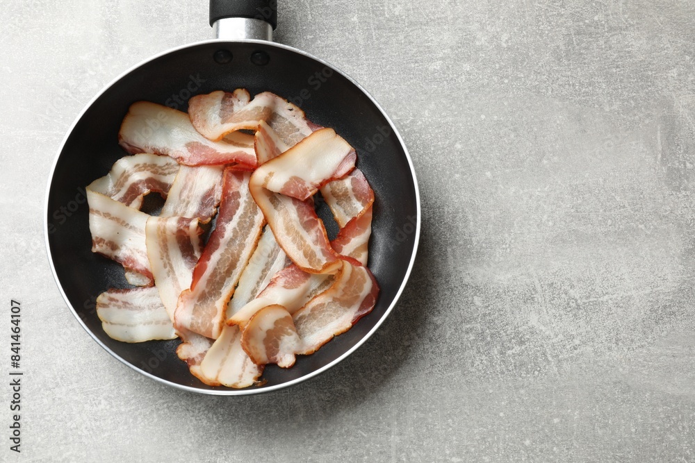 Delicious bacon slices in frying pan on light grey table, top view. Space for text Delicious bacon slices in frying pan on light grey table, top view. Space for text