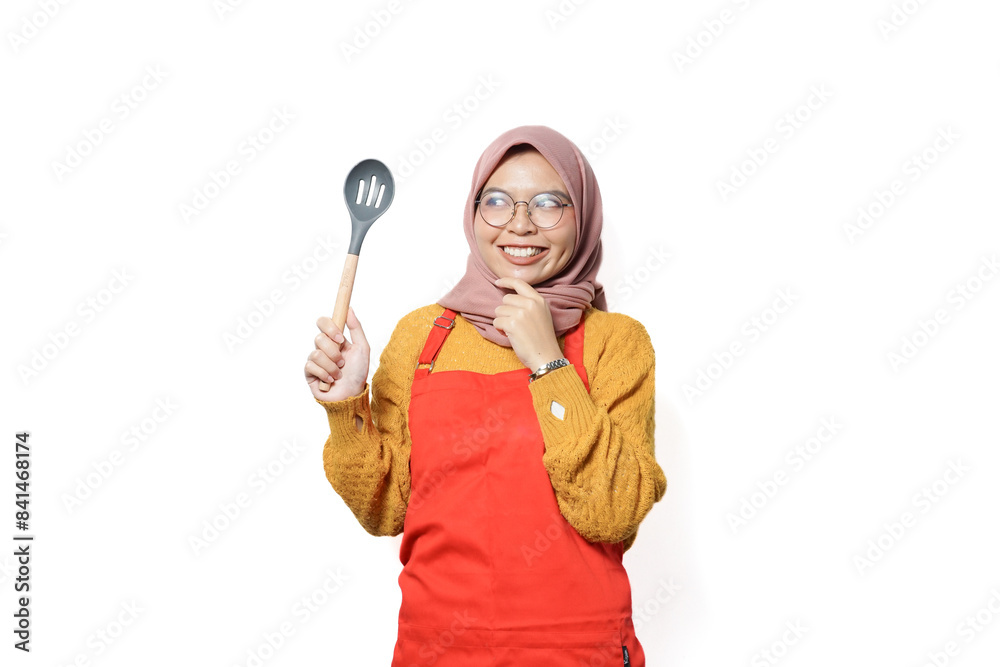 Cheerful asian muslim woman in red apron holding spatula isolated on white Cheerful asian muslim woman in red apron holding spatula isolated on white