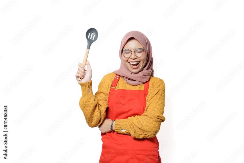 Cheerful asian muslim woman in red apron holding spatula isolated on white Cheerful asian muslim woman in red apron holding spatula isolated on white