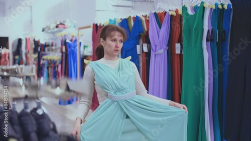 Customer in store has removed hanger with floor-length gown from window and is considering product. Woman client imagines successful new summer outfit photo