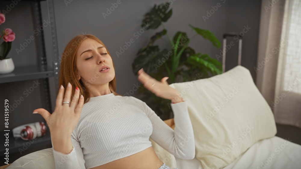 A young woman cooling herself in a modern bedroom setting, conveying a sense of heat and discomfort. A young woman cooling herself in a modern bedroom setting, conveying a sense of heat and discomfort.