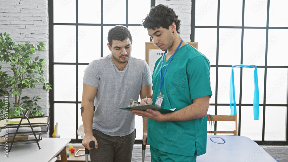 Fototapeta premium A male physiotherapist consulting with a male patient in an indoor rehabilitation clinic.