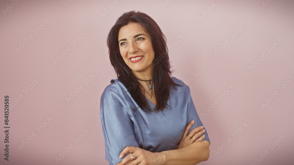 Fototapeta premium Mature hispanic woman with crossed arms smiling against a pink background