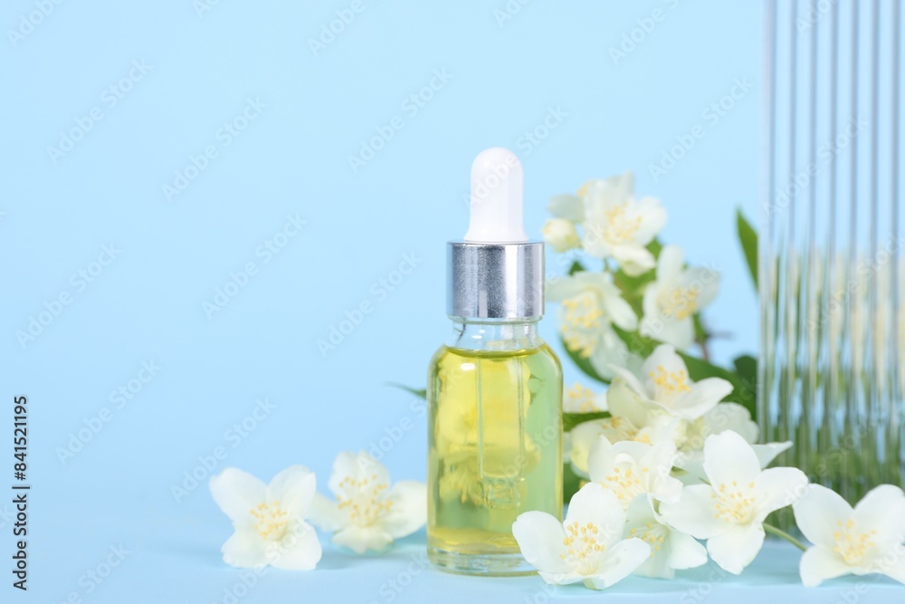 Essential oil in bottle and beautiful jasmine flowers on light blue background, closeup. Space for text Essential oil in bottle and beautiful jasmine flowers on light blue background, closeup. Space for text