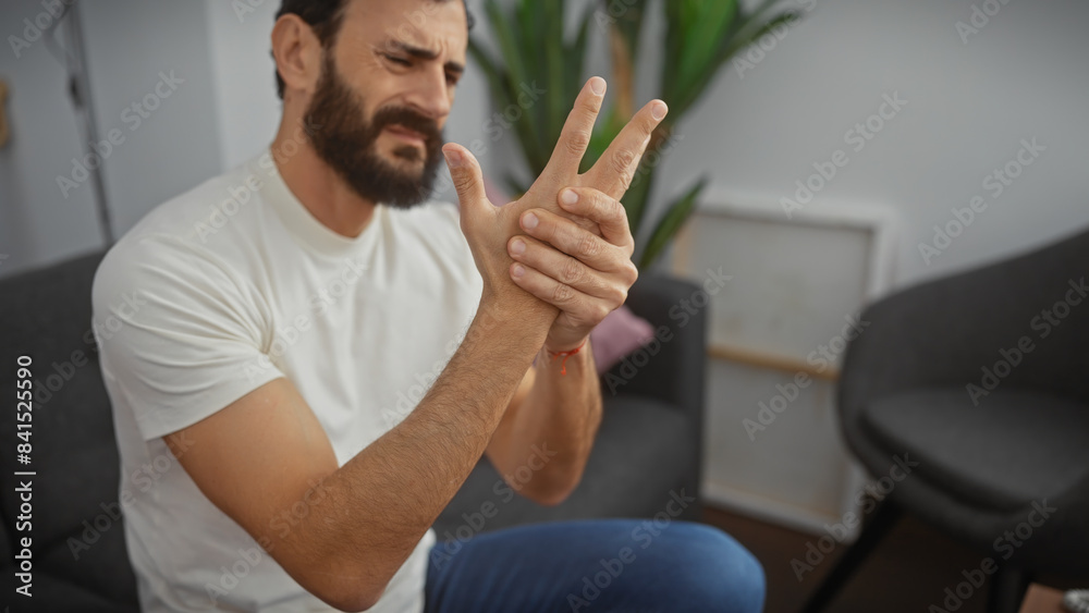 Bearded man experiencing wrist pain indoors, showing discomfort with a pained expression
