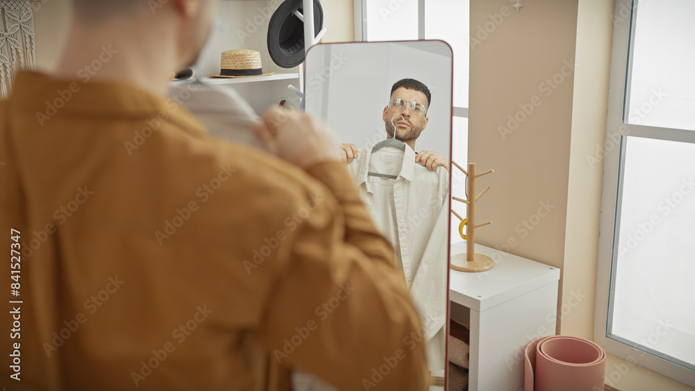 Handsome hispanic man dressing in a fashionable indoor wardrobe room with a mirror Handsome hispanic man dressing in a fashionable indoor wardrobe room with a mirror