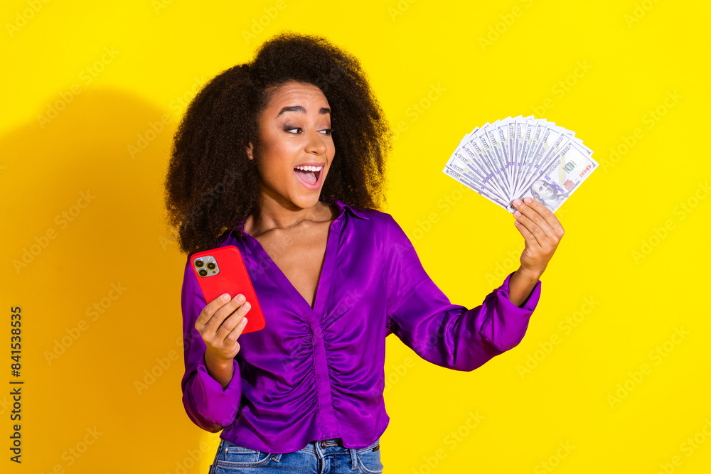 Photo portrait of attractive young woman look excited money fan device dressed stylish violet clothes isolated on yellow color background Photo portrait of attractive young woman look excited money fan device dressed stylish violet clothes isolated on yellow color background