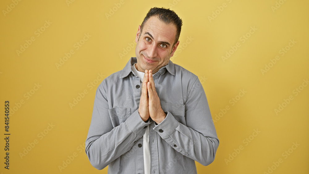 Hispanic man with a pleading expression standing against a yellow background while wearing a gray shirt Hispanic man with a pleading expression standing against a yellow background while wearing a gray shirt