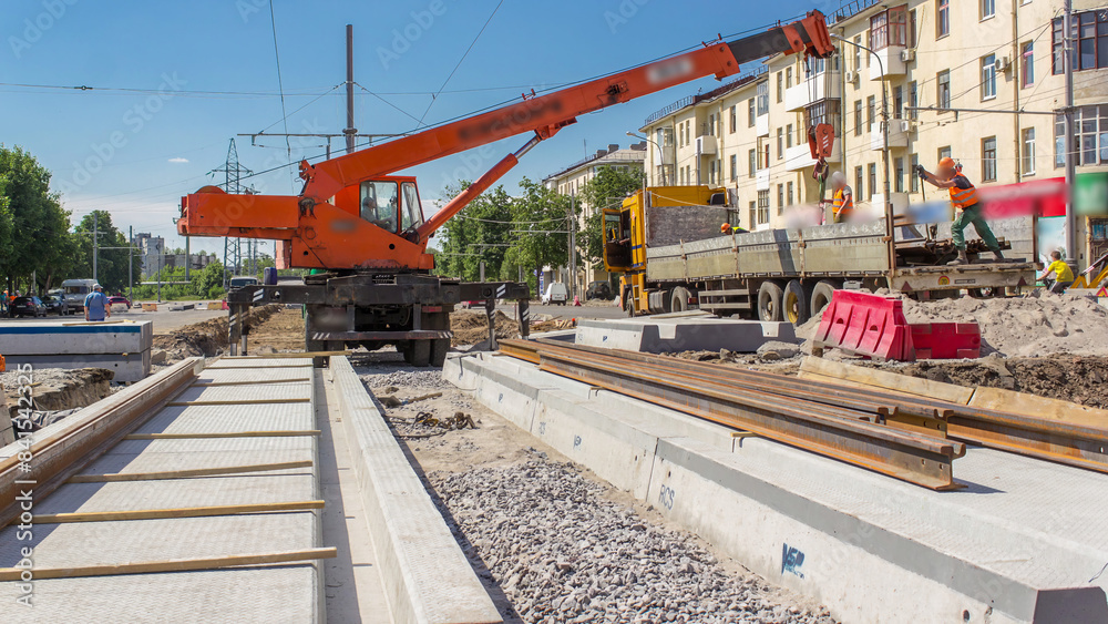 Naklejka premium Orange construction telescopic mobile crane unloading tram rails from truck timelapse.