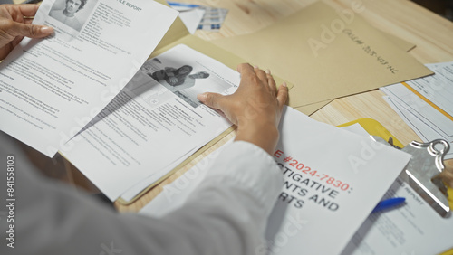 Fotografie A black woman reviews case files at a cluttered police department desk, portraying a sense of investigation and urgency