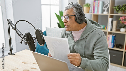 Fotografie Middle-aged man with headphones reading a script indoors at a podcasting studio setup
