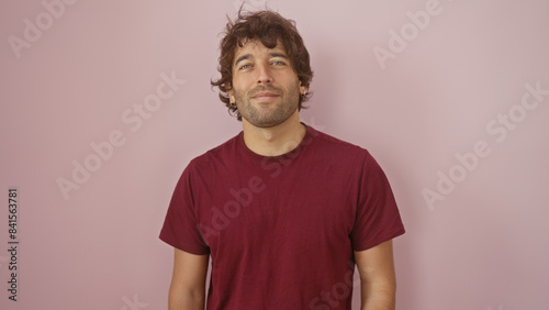 Portrait of a young smiling hispanic man with a beard, wearing a maroon shirt, against a pink wall background. © Krakenimages.com