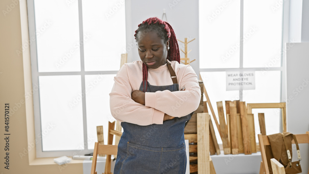 A confident black woman with braids stands arms crossed in a bright carpentry workshop. A confident black woman with braids stands arms crossed in a bright carpentry workshop.