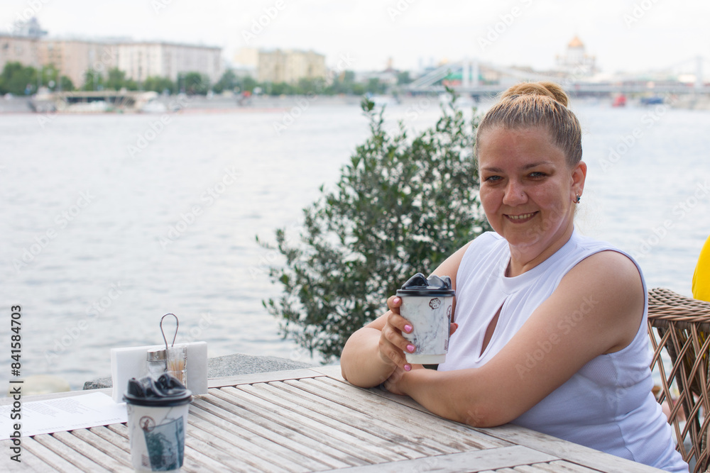 A woman is sitting in a cafe on the embankment and drinking coffee. business woman