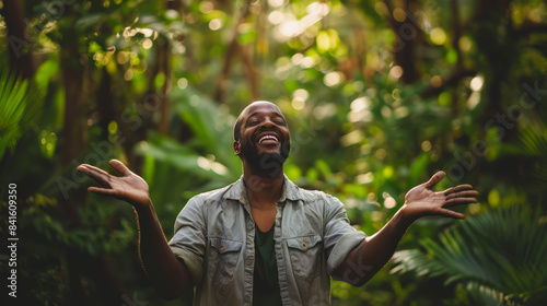 A happy African adult man standing with his arms open freely in the forest being relaxed and enjoying the nature, greenery of the jungle