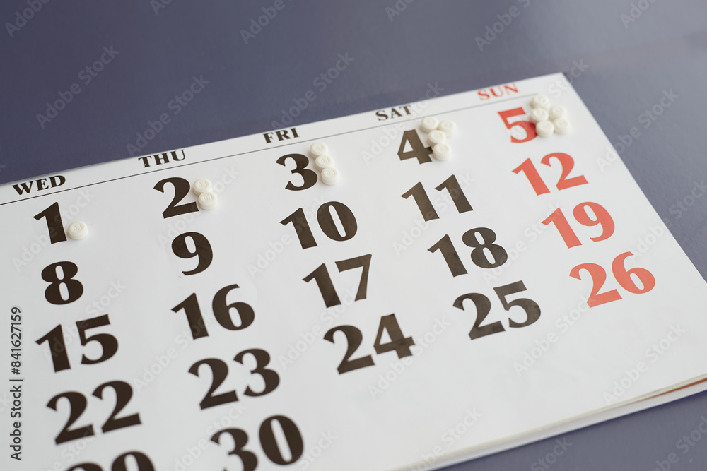 Obraz premium Tagged white pills on calendar closeup, increasing dose of medication by day, increasing dose of medication, daily medication, increasing dose of medication