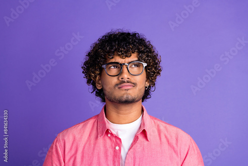 Portrait of nice young man look empty space think wear pink shirt isolated on purple color background