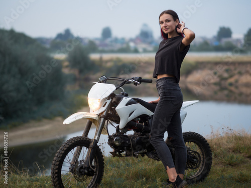 a young woman poses near a cross-country motorcycle in nature