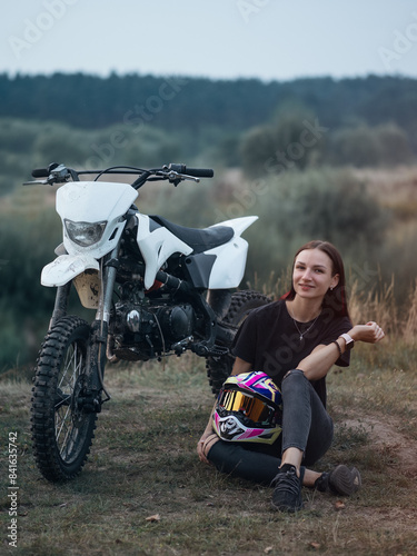 A young woman is sitting near a cross-country motorcycle
